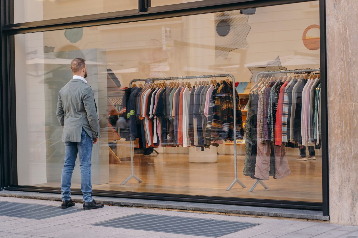 Person looking at a display of clothes through a large shop window, where various shirts are displayed on shelves.