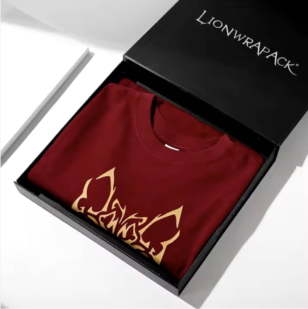 A red T-shirt with gold graphics is neatly folded inside a black box with the Lionwrapack logo.